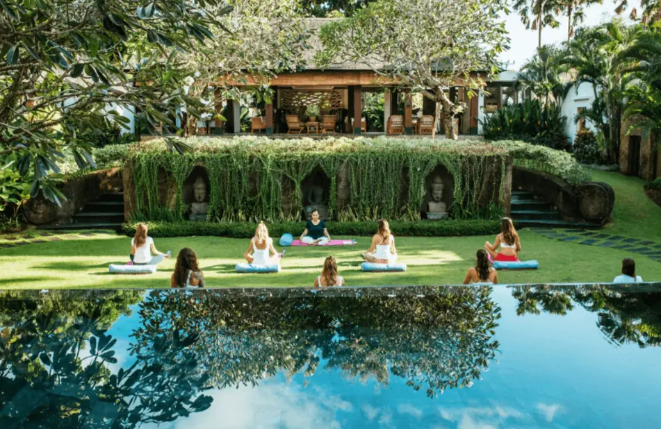 A group of people sitting in the grass near water.