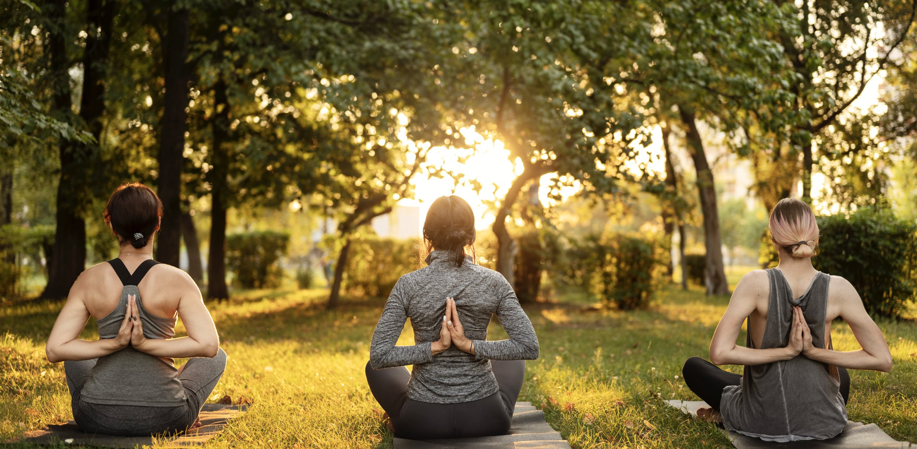 A woman is sitting in the grass doing yoga.